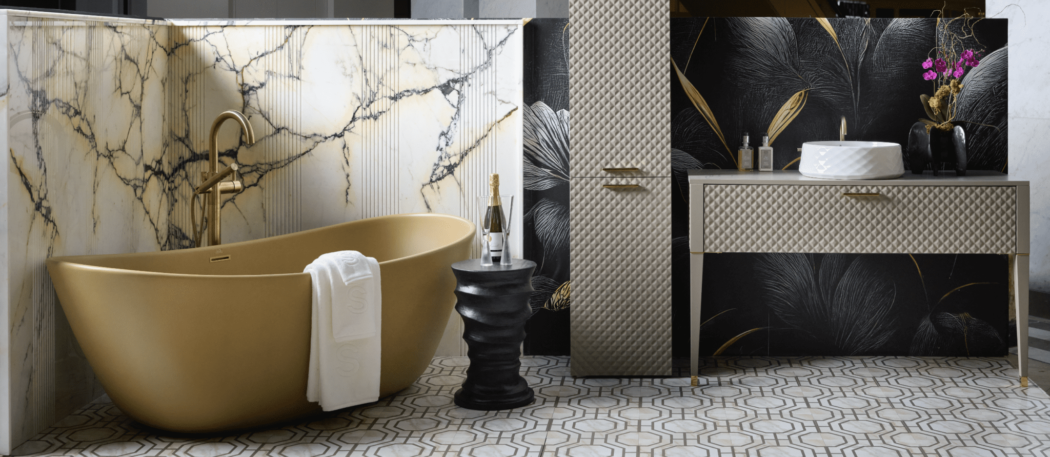 Gold bathtub with brass faucet, black sculptural side table with champagne, and vanity with white